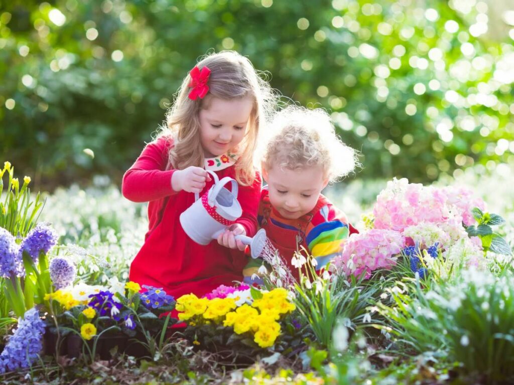 Two young children are in a garden, surrounded by colorful flowers.