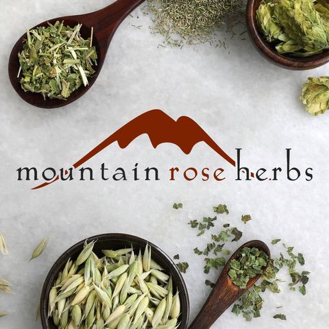 Four wooden spoons filled with various herbs surrounding the logo of "Mountain Rose Herbs," featuring a stylized mountain graphic, perfectly captures the essence of an easy homemade life.