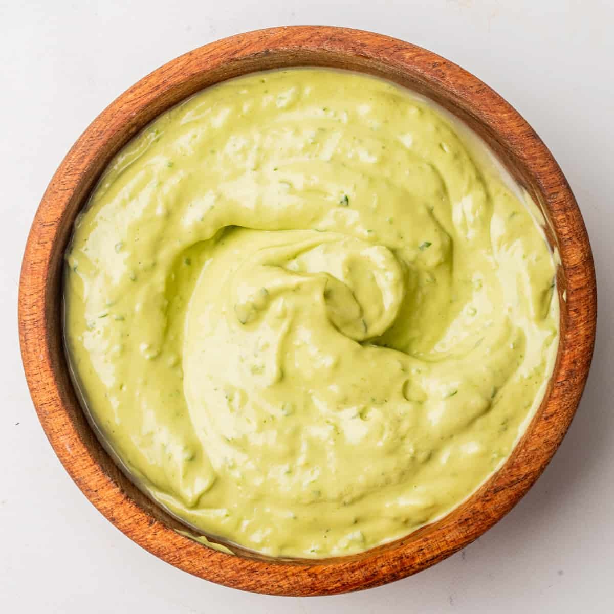 A wooden bowl filled with smooth, creamy green avocado dip.