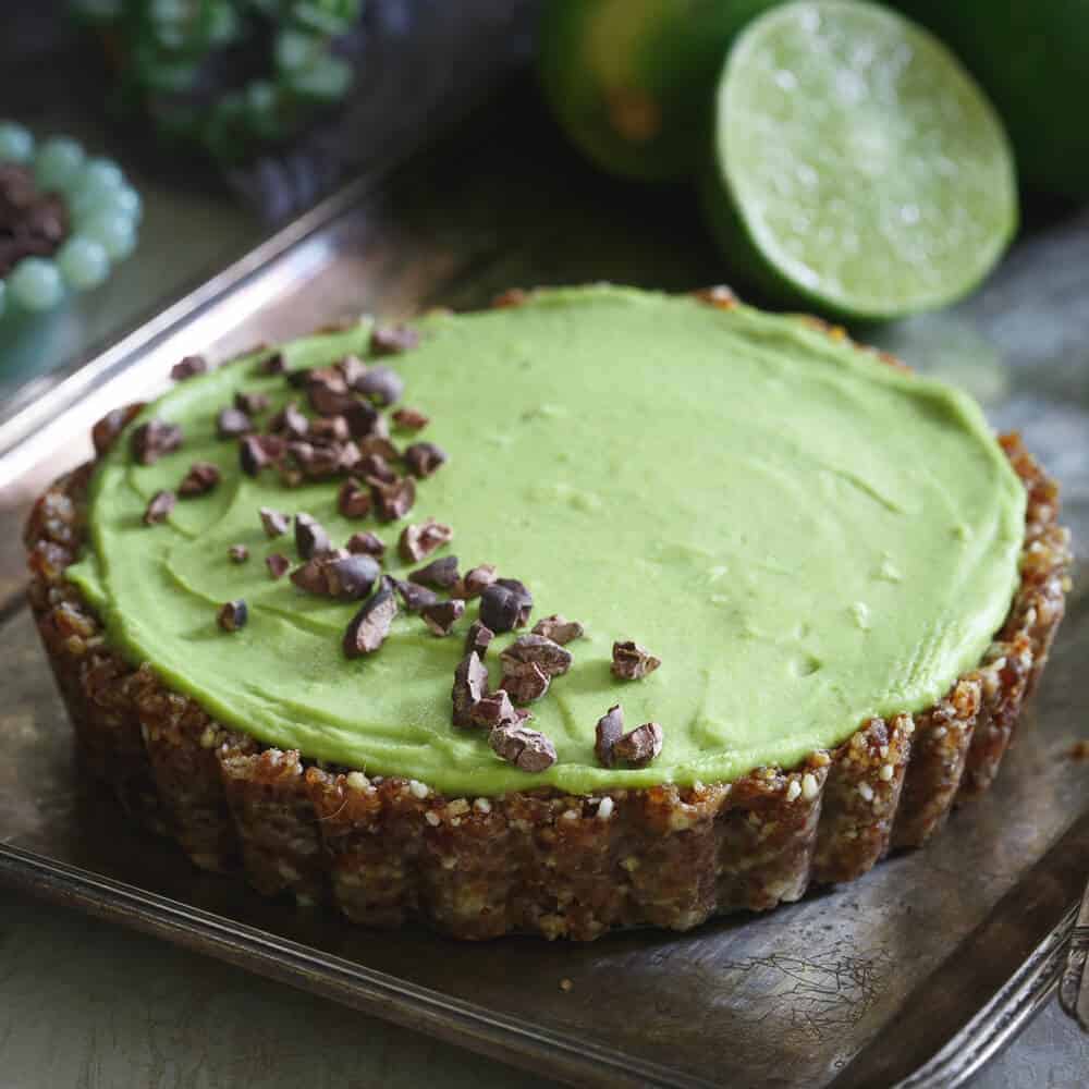 A green tart garnished with chocolate pieces on one side, resting on a silver tray.