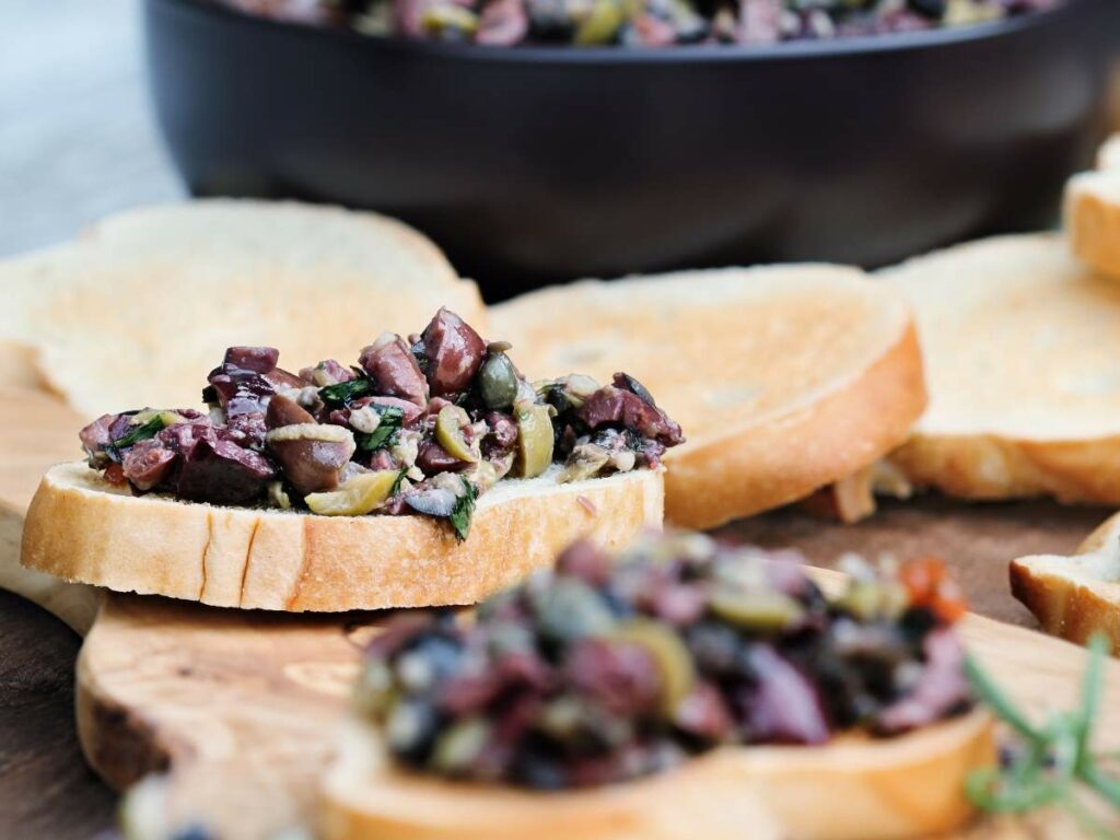 A close-up of toasted bread slices topped with a chopped olive and herb mixture.