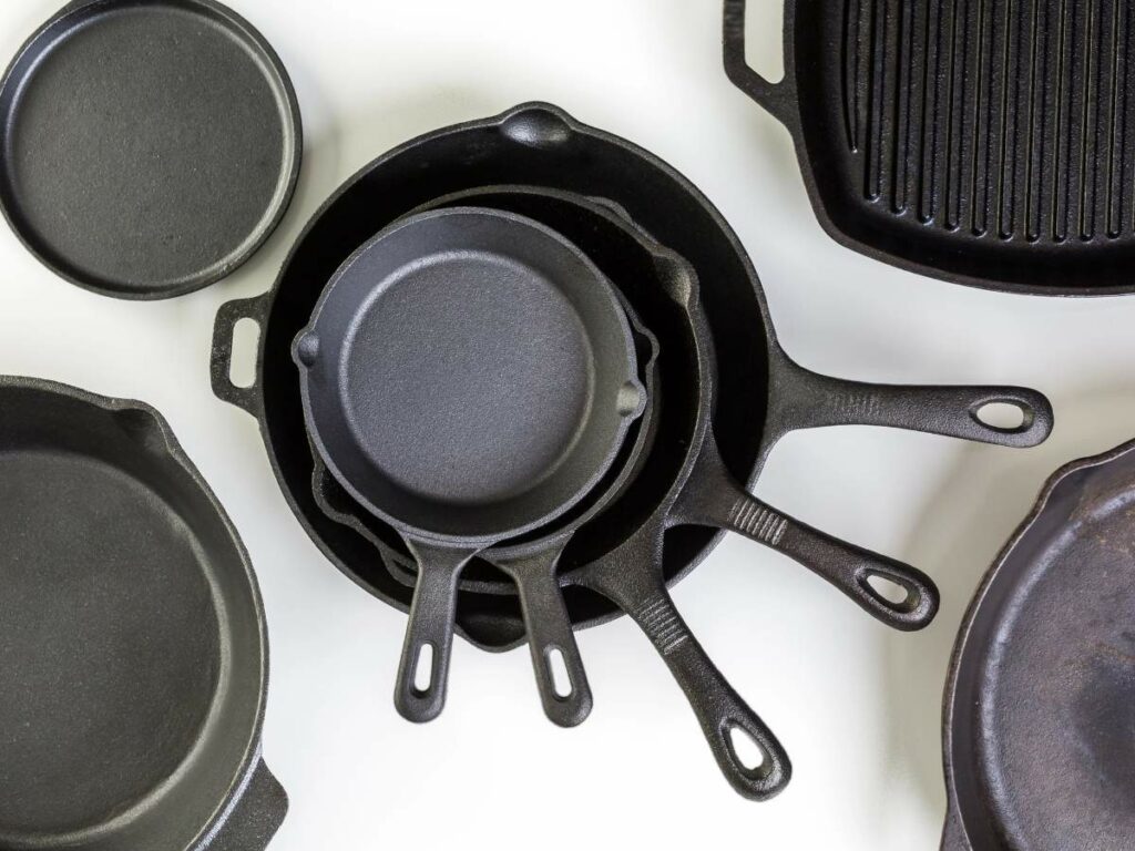 A collection of cast iron cookware, including skillets of various sizes, a grill pan, and a griddle, arranged on a white surface.