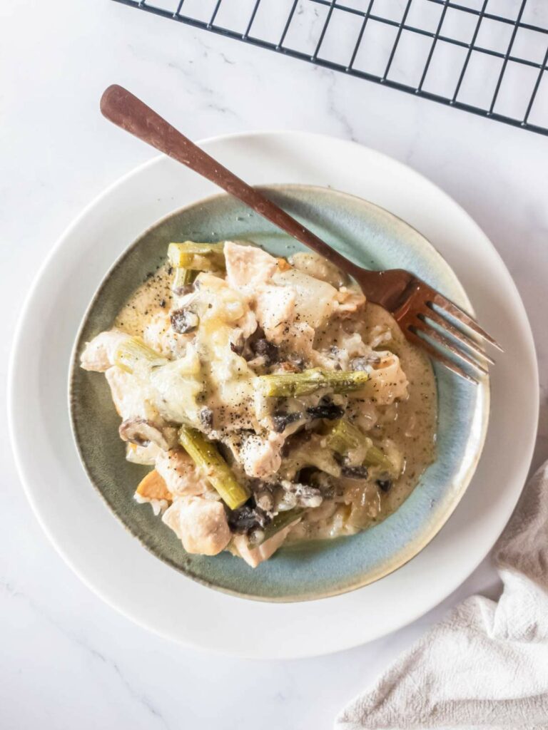 A plate of creamy chicken asparagus casserole with vegetables, placed on a white surface.