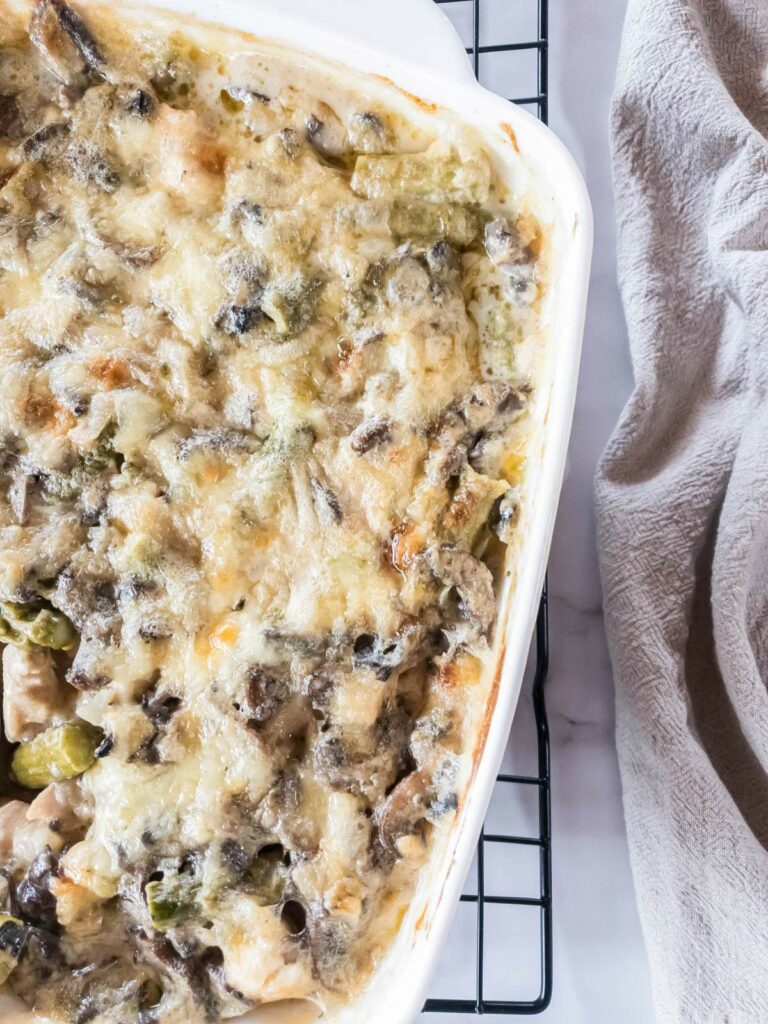 Chicken asparagus casserole in a white dish, featuring a melted cheese topping with visible pieces of vegetables and mushrooms.