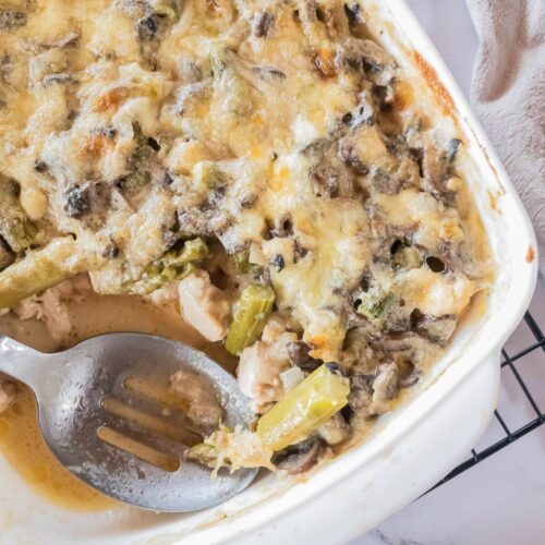 A dish filled with chicken asparagus casserole, partially served with a serving spoon resting inside.