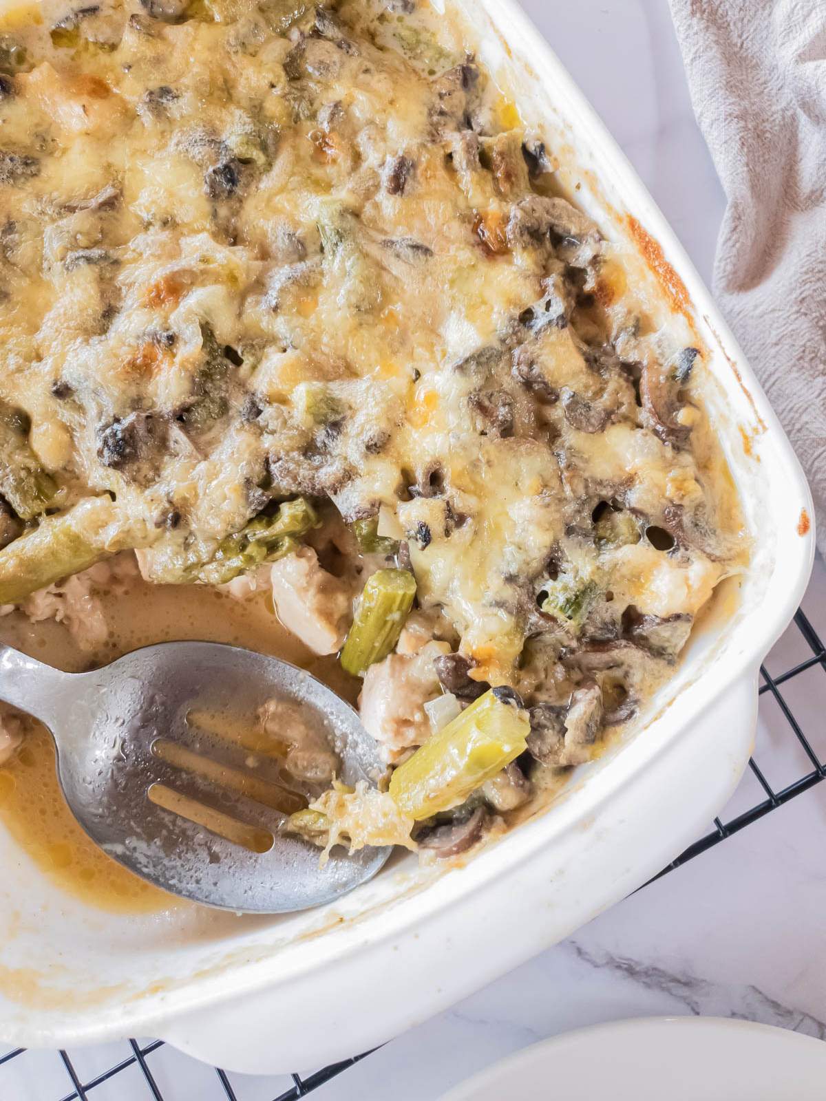 A dish filled with chicken asparagus casserole, partially served with a serving spoon resting inside.