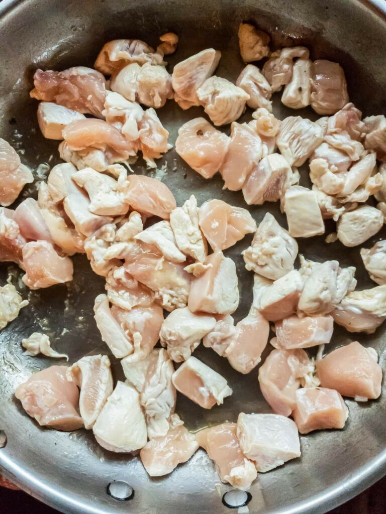 Raw, cubed chicken pieces in a metal pan, ready to be cooked.