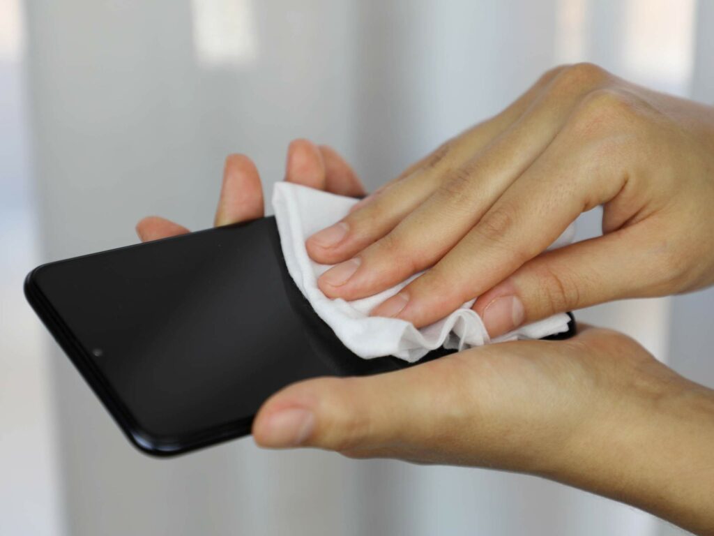 A person cleans a smartphone screen with a white cloth.