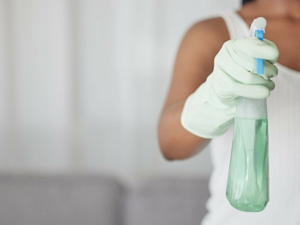 Person in gloves holding a spray bottle filled with cleaning solution.