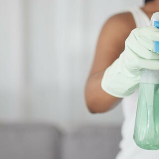 Person in gloves holding a spray bottle filled with cleaning solution.