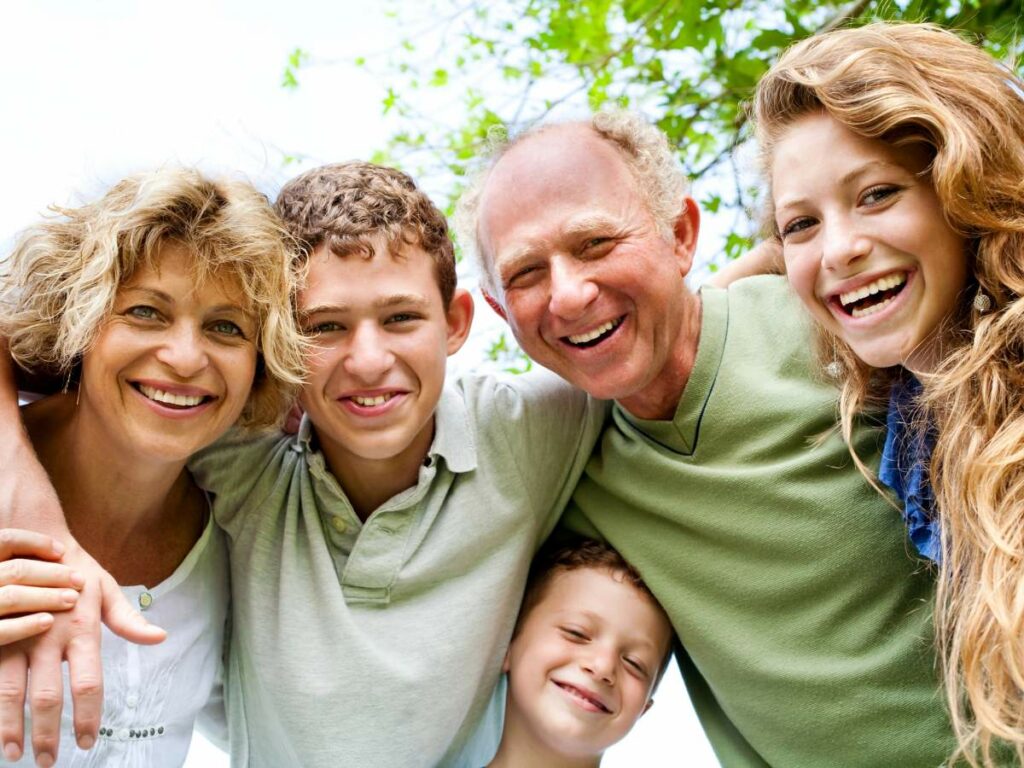 A family of five, including two adults and three children, smiling and hugging outdoors.