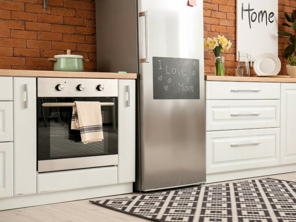 A modern kitchen with white cabinets, a stainless steel refrigerator, an oven with a towel, and a countertop with decor and a pot.