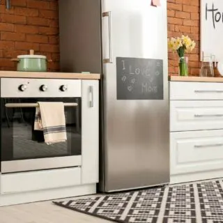 A modern kitchen with white cabinets, a stainless steel refrigerator, an oven with a towel, and a countertop with decor and a pot.
