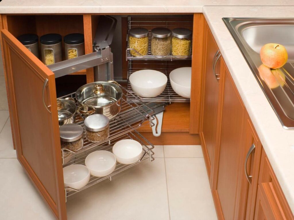 Corner kitchen cabinet with pull-out shelves containing various pots, bowls, and jars.