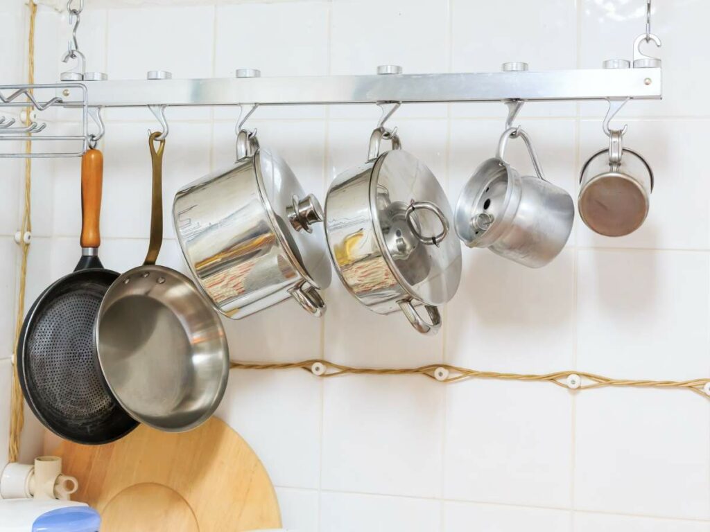 A wall-mounted rack holds various metal pots, pans, and kettles hanging by hooks.