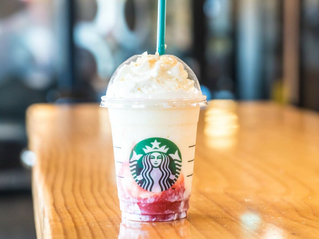 A Starbucks frappuccino with whipped cream and red syrup sits on a wooden table.