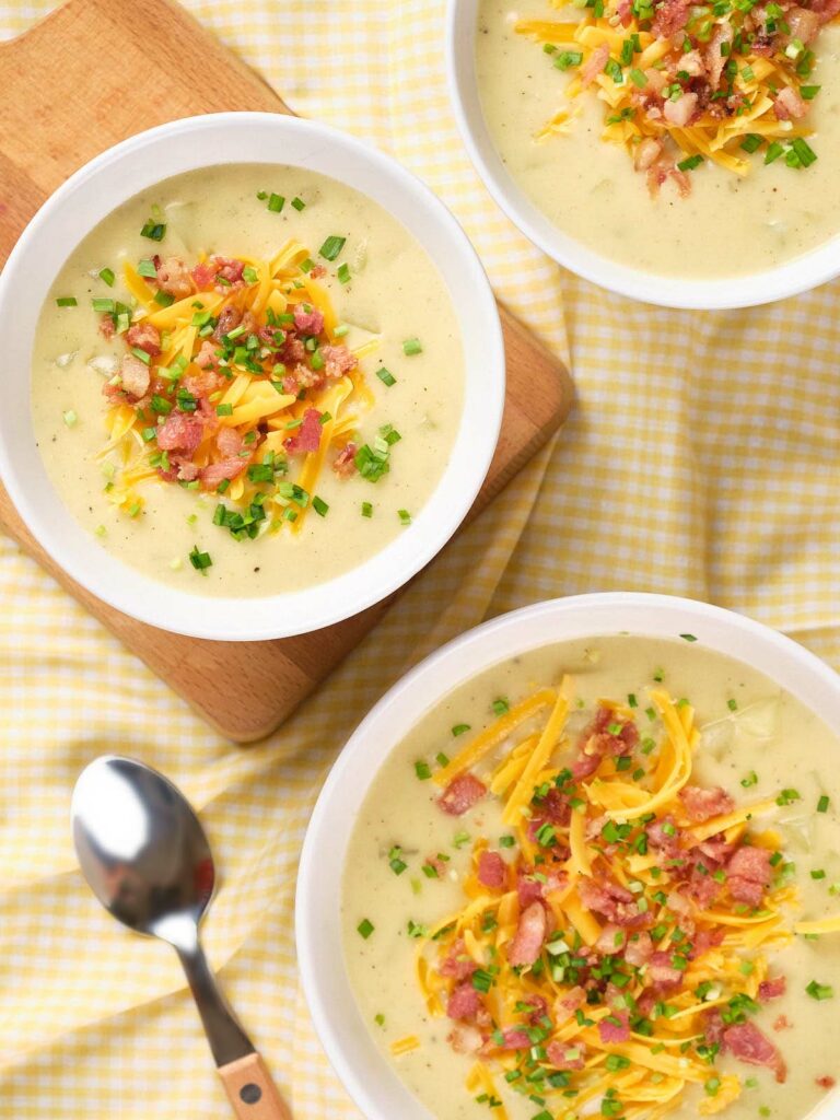 Three bowls of baked potato soup on a checkered tablecloth.