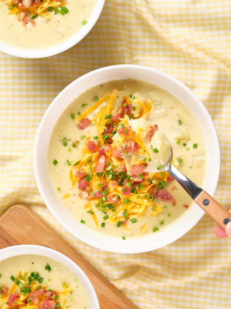 A bowl of creamy baked potato soup with a spoon lifting a portion of the soup.