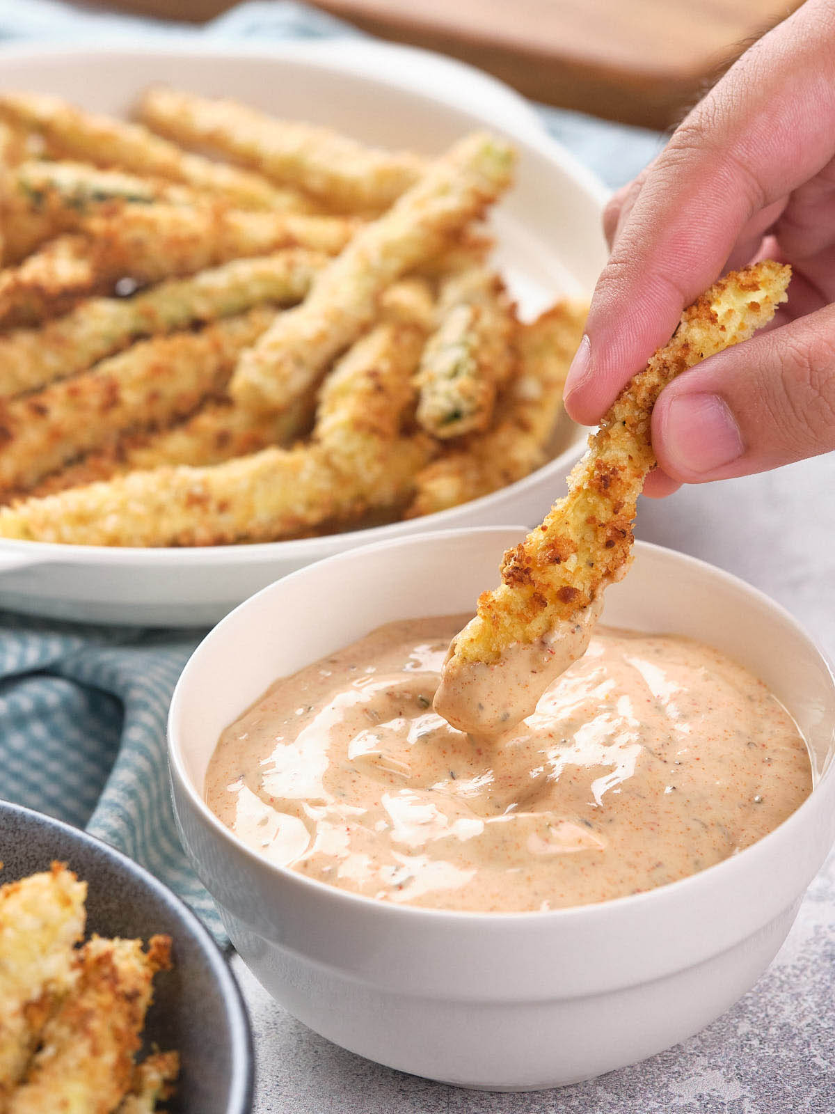 A hand dipping a fried zucchini fry into a blackened ranch sauce.