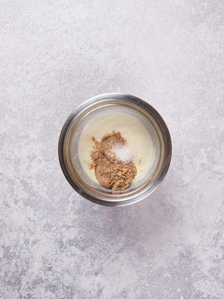 Stainless steel bowl containing a light-colored mixture, topped with brown and white powder.