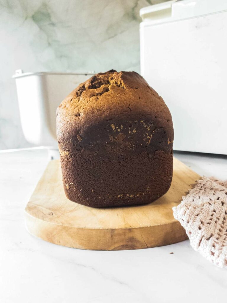 A loaf of pumpkin bread with a dark brown crust sits on a wooden cutting board.