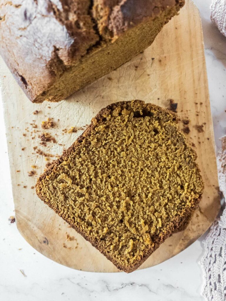 A loaf of pumpkin bread sits on a wooden cutting board with one slice cut off.