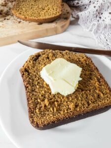 A slice of pumpkin bread with a pat of butter on a white plate.