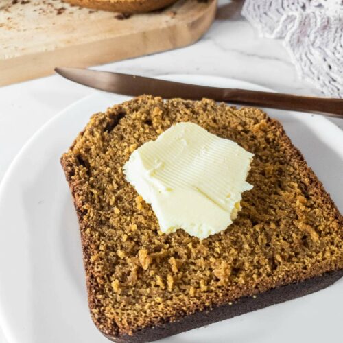 A slice of pumpkin bread with a pat of butter on a white plate.