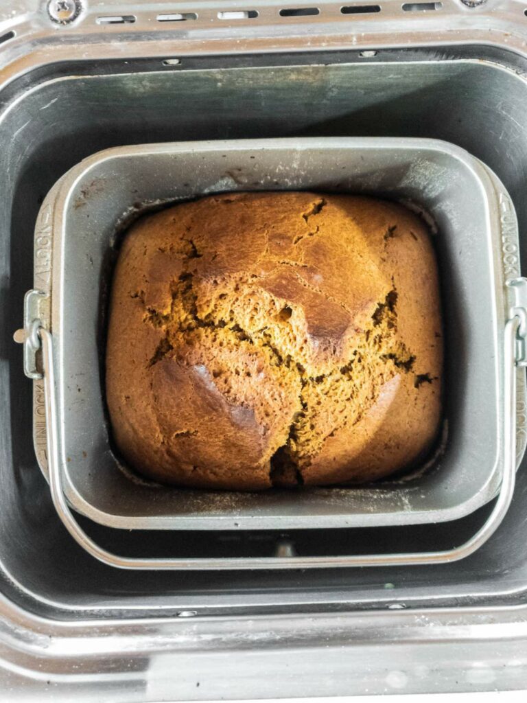 A loaf of pumpkin bread with a golden-brown crust sits in a bread machine pan.