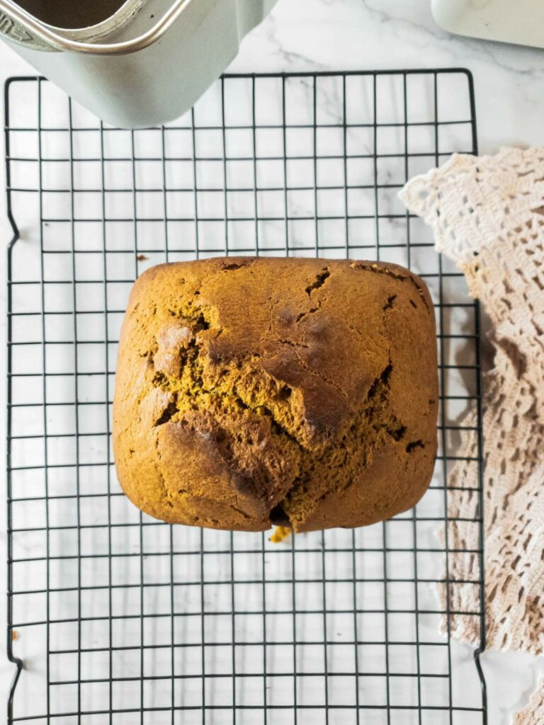 A freshly baked loaf of pumpkin bread cooling on a wire rack next to a lace cloth.