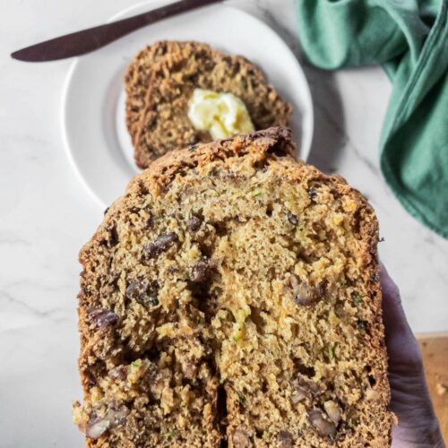 Close-up of a hand holding a slice of zucchini bread.