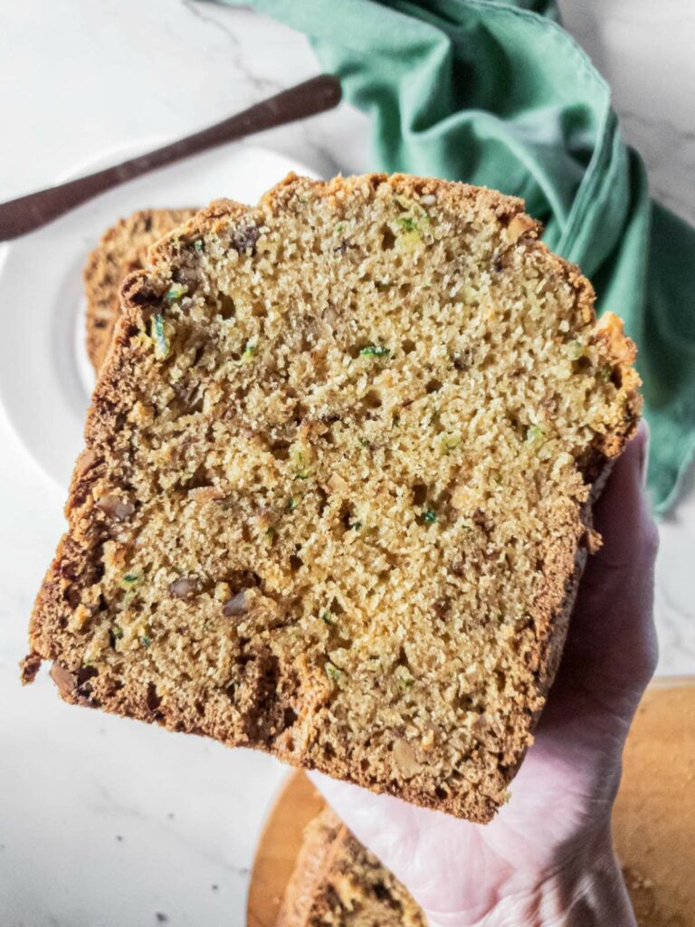 A close-up of a hand holding a slice of homemade zucchini bread.