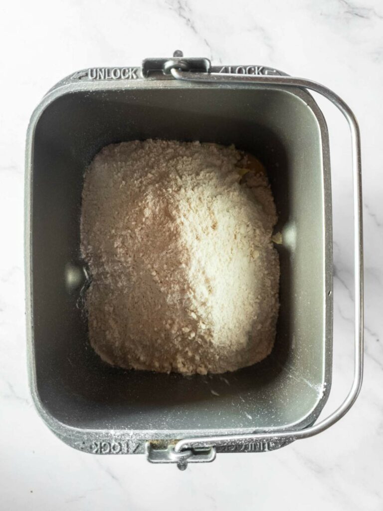 A bread machine pan contains a mixture of flour and other dry ingredients.