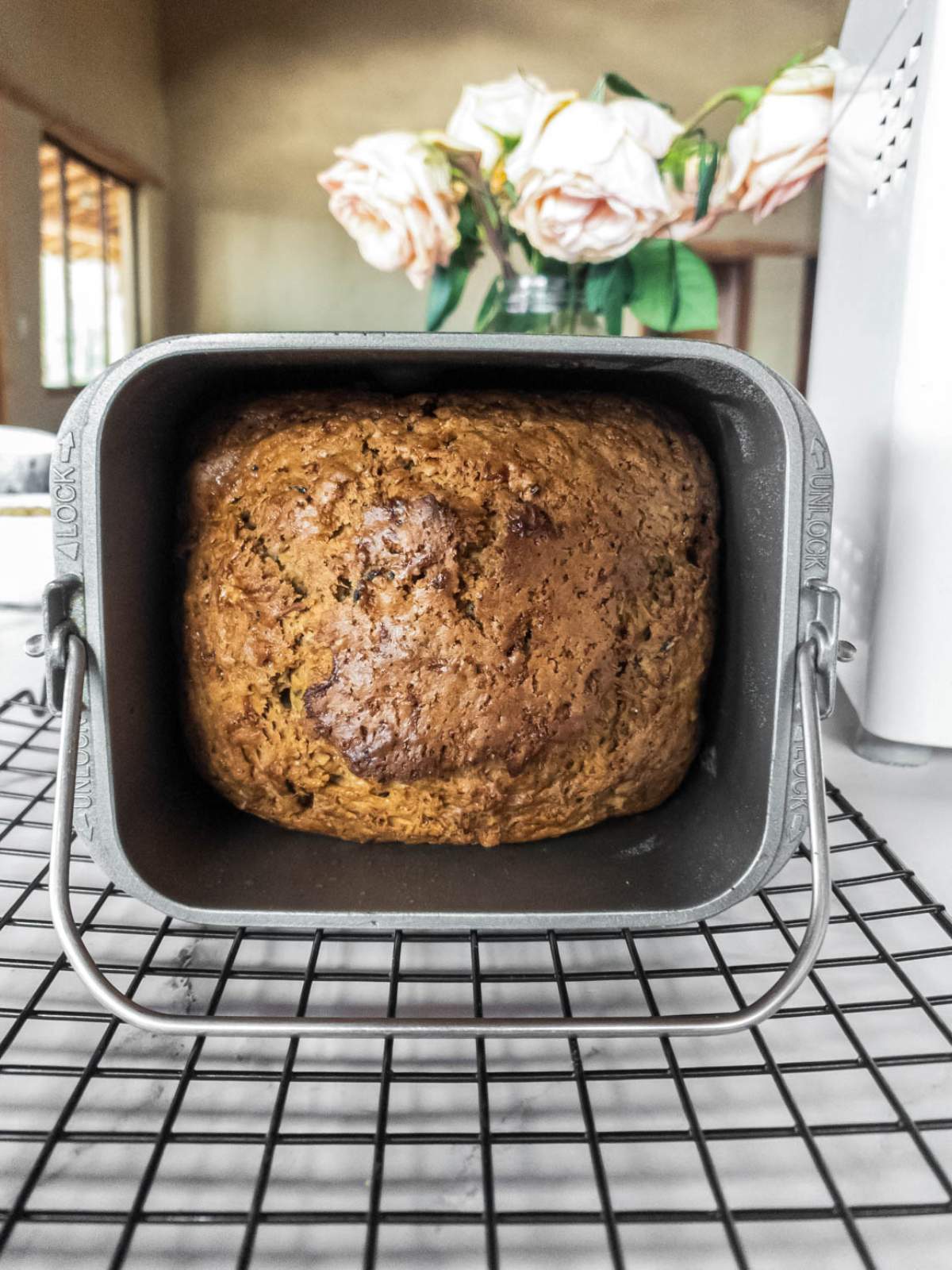 A loaf of freshly baked zucchini bread in a bread pan sits on a cooling rack.