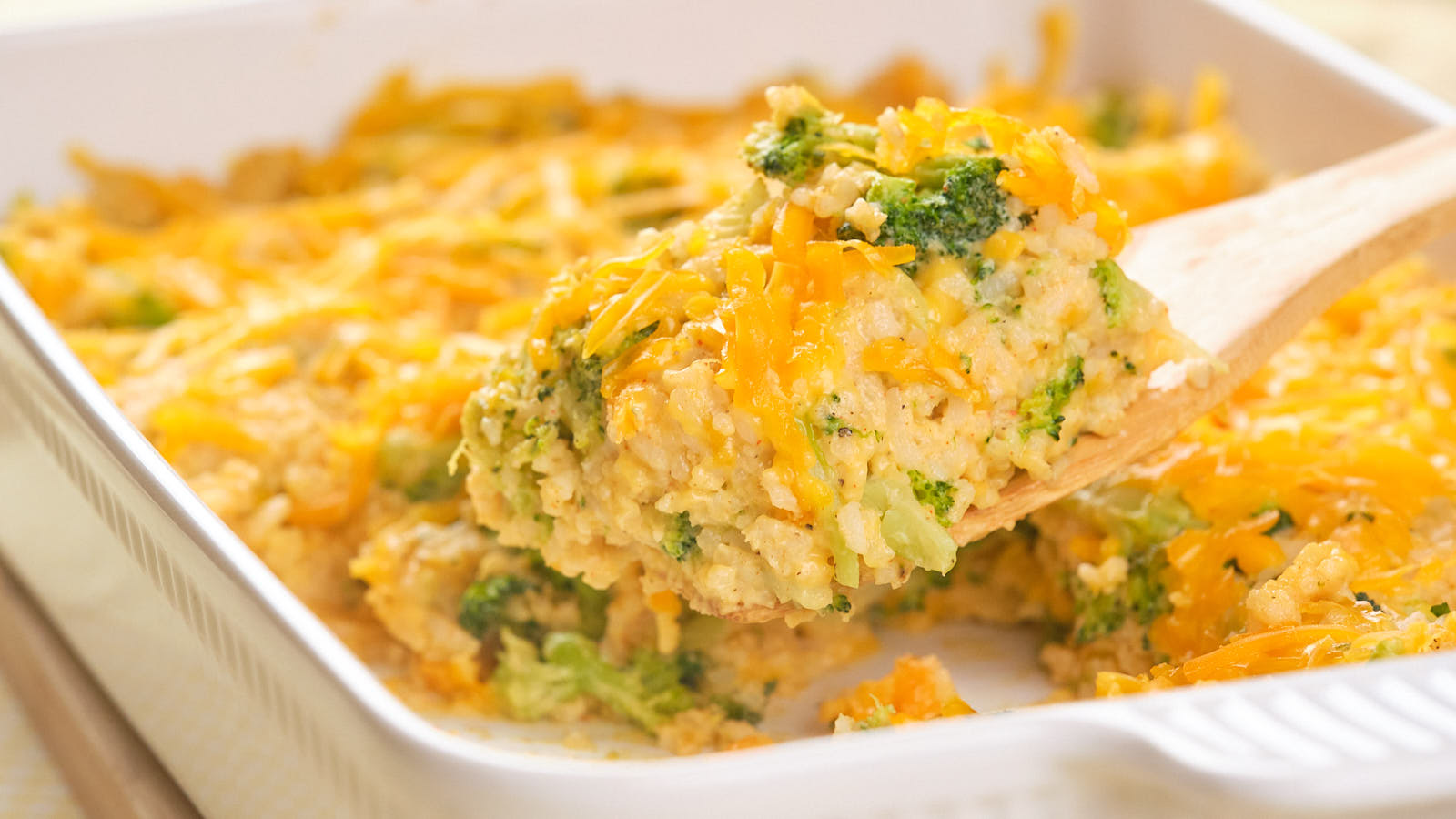 A wooden spoon holds a serving of broccoli rice casserole from a baking dish.