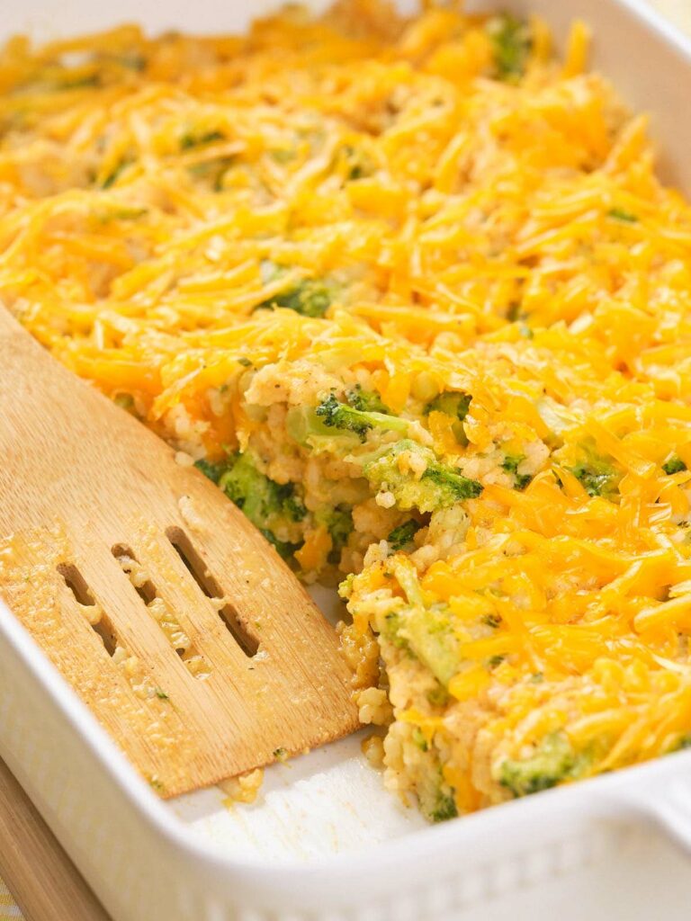 A partially served broccoli rice casserole with a wooden spatula in a white baking dish.