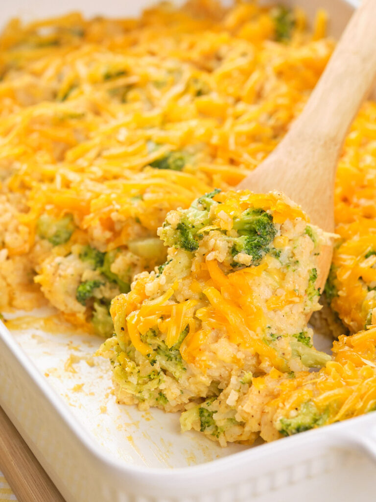 A wooden spoon scooping a serving of broccoli rice casserole.