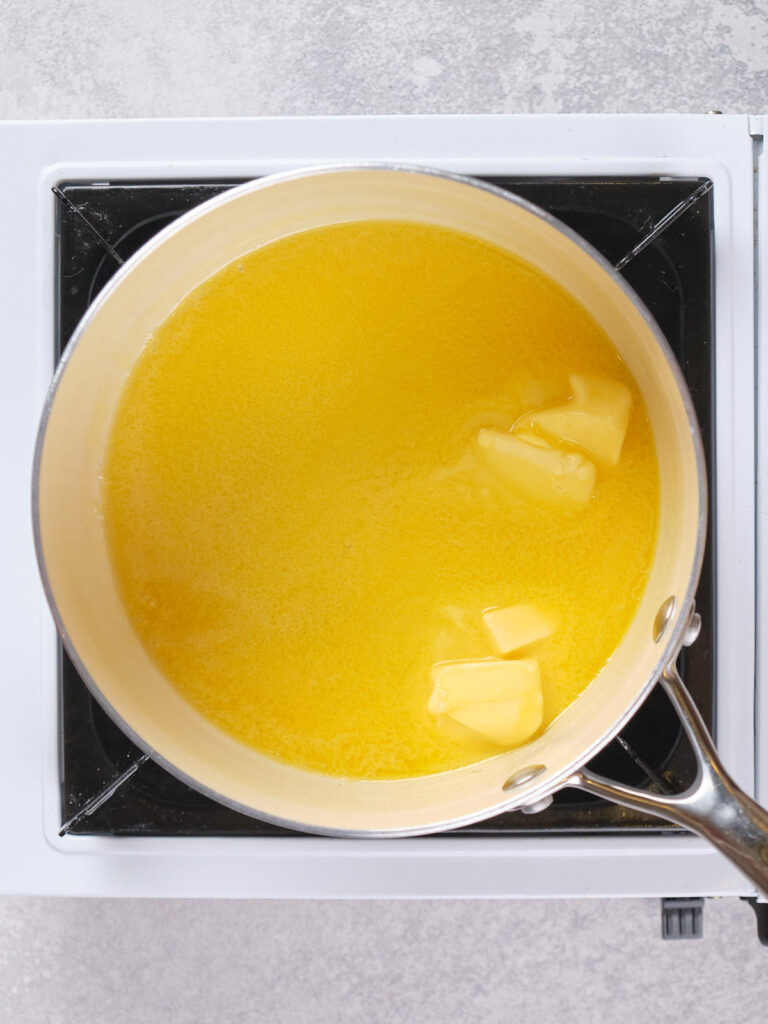 A saucepan on a stove contains melted and partially melted butter.