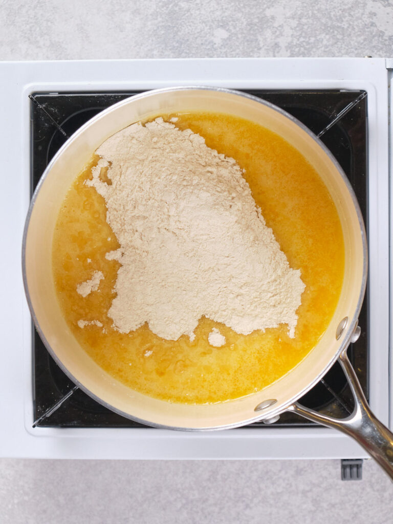 A saucepan on a stove contains melted butter topped with a pile of dry ingredients.