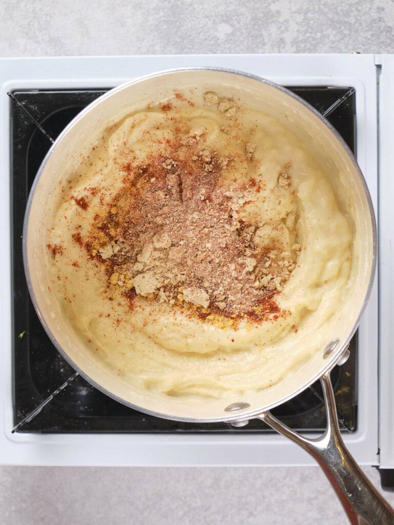 A pot of wet mixture on a stove, topped with spices and seasoning.