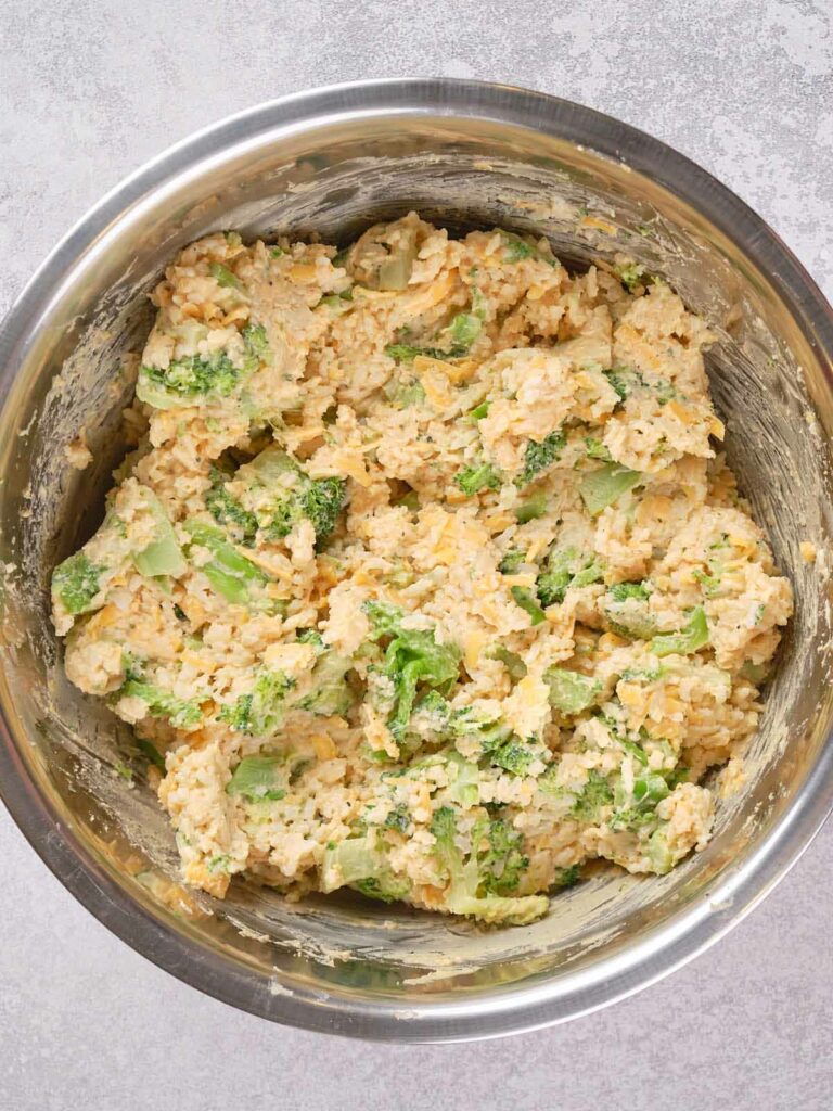 A mixing bowl filled with a mixture of rice, broccoli, cheese, and a creamy sauce.