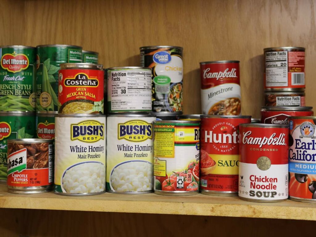 A variety of canned foods arranged on wooden pantry shelves.