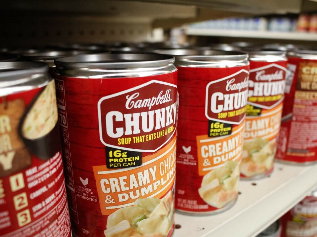 Rows of Campbell's Chunky Creamy Chicken & Dumpling canned soup on a grocery store shelf.