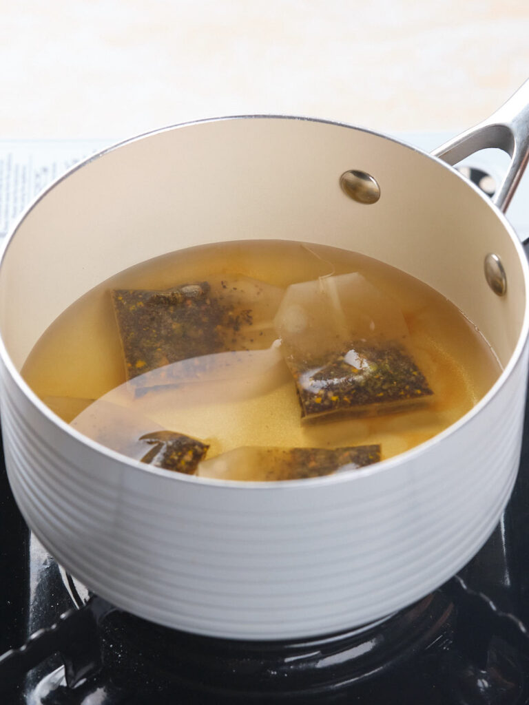 A white pot on a stove contains simmering water and several tea bags.