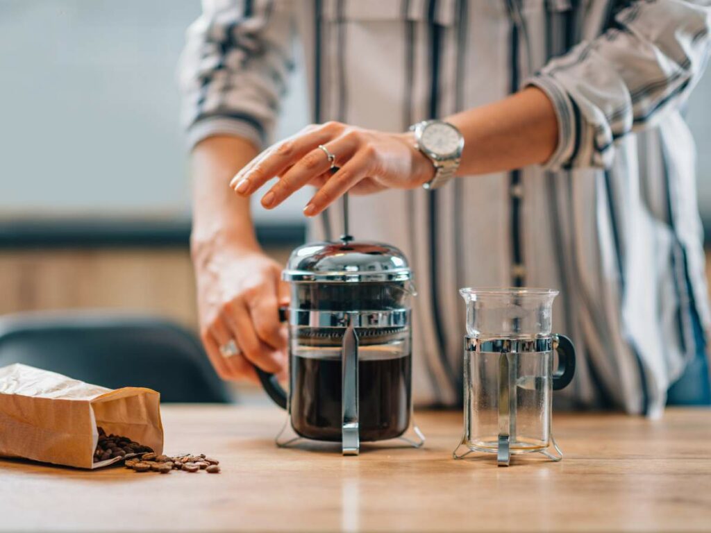 A person wearing a striped shirt presses down the plunger of a French press filled with coffee.