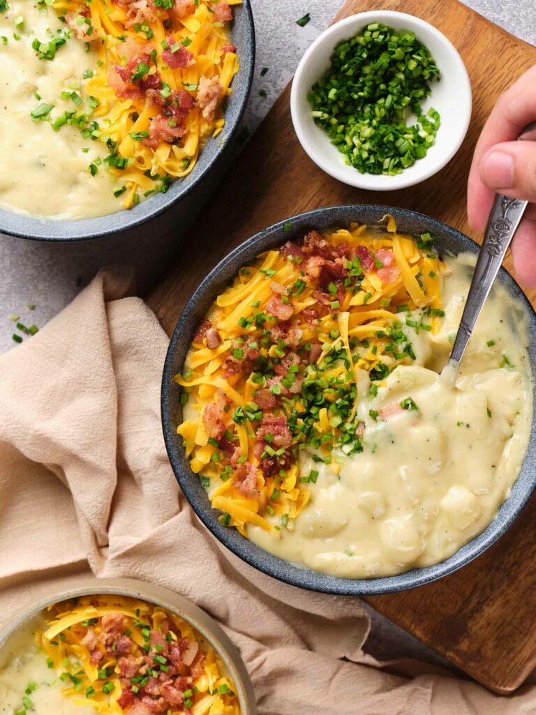 Top-down view of two bowls of loaded potato soup with cheese, bacon, and chives.