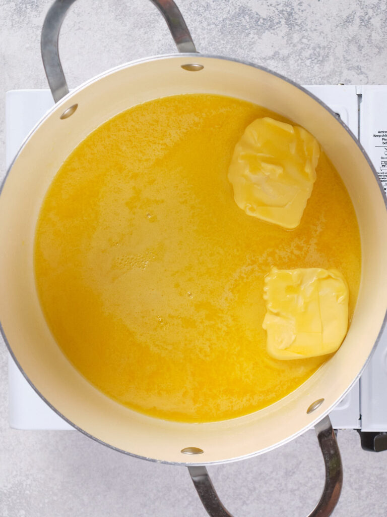 A pot on a stove containing melted butter with two remaining solid chunks.