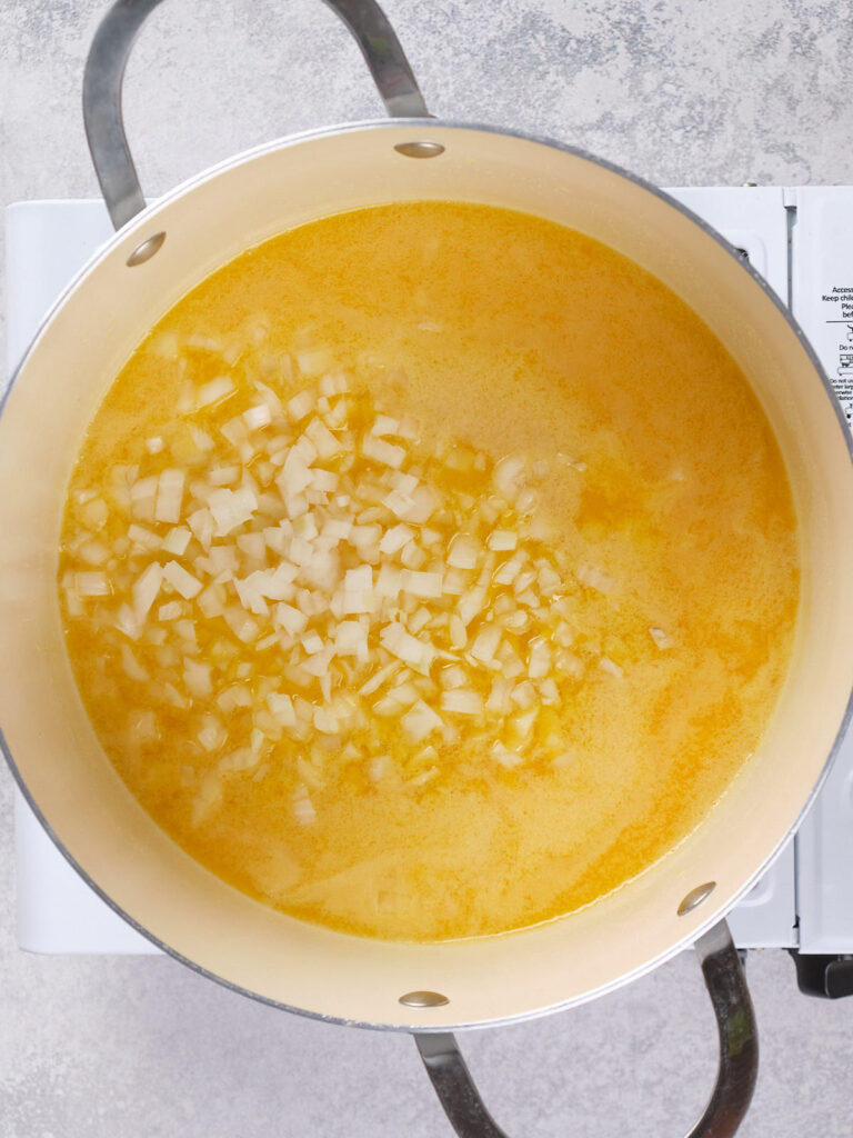 A pot filled with a melted butter and chopped onions cooking on a stovetop.