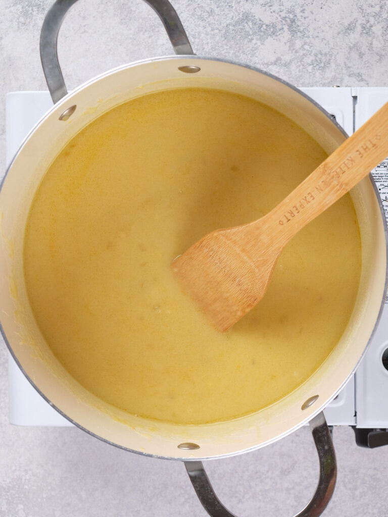 A pot filled with creamy soup being stirred with a wooden spatula on a countertop.