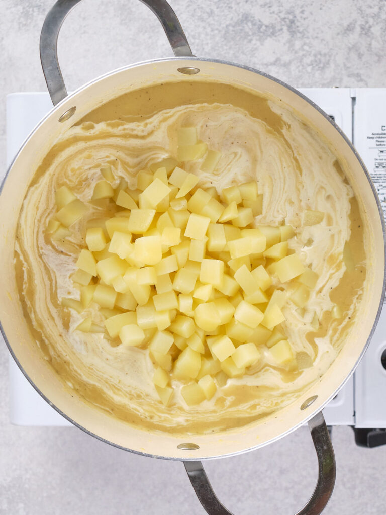 A pot containing a cream-based liquid with diced potatoes, placed on top of a stove.